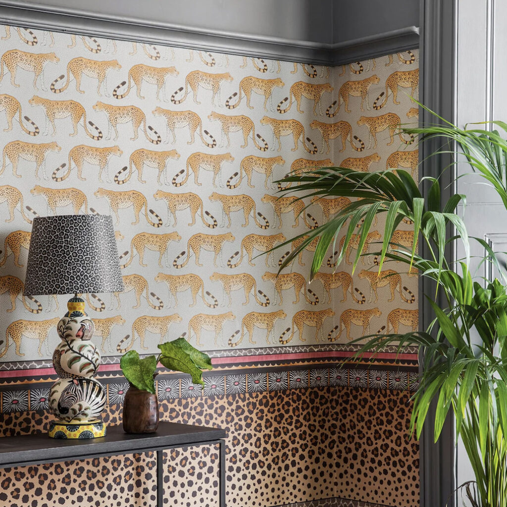 Interieurhoek met Cole and Son Leopard Walk behang, een tropische plant en een decoratieve lamp op een tafel.