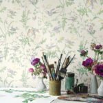 Kunstzinnige werkplek met bloemen, schildermaterialen en Cole & Son-behang Hummingbirds in pasteltinten op de achtergrond.