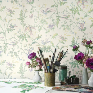 Kunstzinnige werkplek met bloemen, schildermaterialen en Cole & Son-behang Hummingbirds in pasteltinten op de achtergrond.