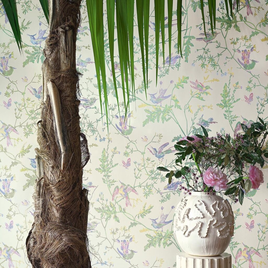 Sfeervolle interieursetting met Cole & Son Hummingbirds-behang, een palmbomenstam en een vaas met bloemen.