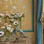 Decoratieve opstelling met glazen vaasjes vol anemonen, twee porseleinen parkieten en Cole & Son Hummingbirds-behang op de achtergrond.