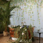 Koperen badkuip met bloemen en klimop in een botanisch interieur met Cole & Son Hummingbirds Flora-behang.