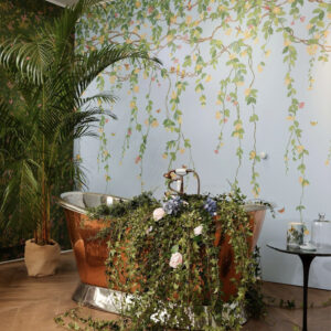 Koperen badkuip met bloemen en klimop in een botanisch interieur met Cole & Son Hummingbirds Flora-behang.
