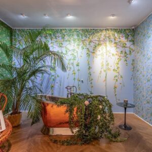 Sfeervolle badkamer met koperkleurig bad en Cole & Son Hummingbirds Flora-behang met kleurrijke bloem- en vogelmotieven.