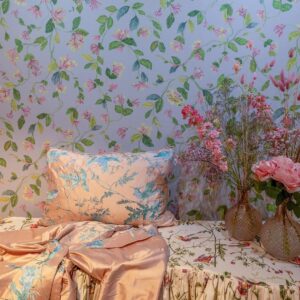 Zijaanzicht van een romantisch interieur met Cole & Son Hummingbirds-behang en bijpassende stof in zijdezachte pastelkleuren, omlijst door bloemen in vazen.