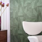 Moderne interieurhoek met EArte Essentials Tangram Caprice behang in groen patroon, een witte designstoel en een paarse vaas met bloemen.