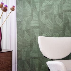 Moderne interieurhoek met EArte Essentials Tangram Caprice behang in groen patroon, een witte designstoel en een paarse vaas met bloemen.
