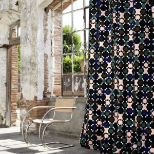 Gordijn van ELITIS-stof met kleurrijk geometrisch patroon hangt in een vervallen industriële ruimte met bakstenen muur en metalen stoel.