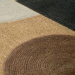 Detailopname van het Elitis Acapulco vloerkleed met geweven texturen en geometrische kleurvlakken in bruin, beige, zwart en crème.