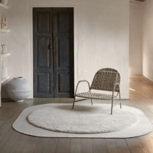 Sfeervolle interieursetting met het Elitis Alaska TA 125 03 07 vloerkleed, een rotan stoel en rustieke dubbele houten deuren.