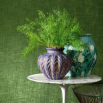 Twee decoratieve vazen met groene planten op een wit marmeren tafeltje tegen een groene Elitis Alcove RM 410 63 behangachtergrond.