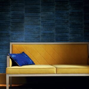 Mosterdgele bank met een blauw sierkussen tegen een donkerblauwe Elitis Anguille-4 wandbekleding.