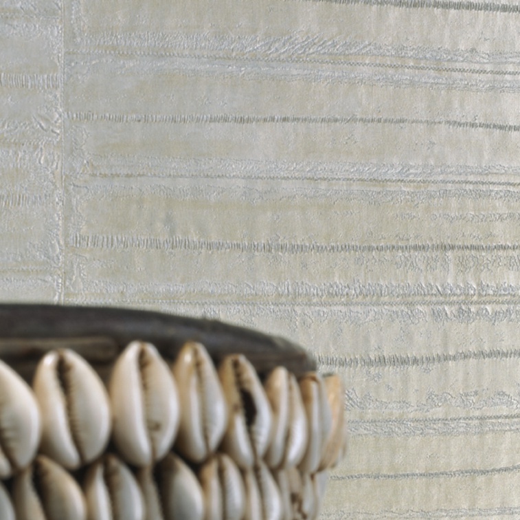 Detail van Elitis-Anguille-8 behang met een glanzende textuur in lichte tinten en een decoratieve schaal met kaurischelpen op de voorgrond.