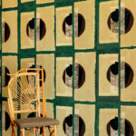 Rieten stoel voor een wand met grafisch Elitis Izu RM 1030 05 behang met geometrisch patroon in aardetinten.
