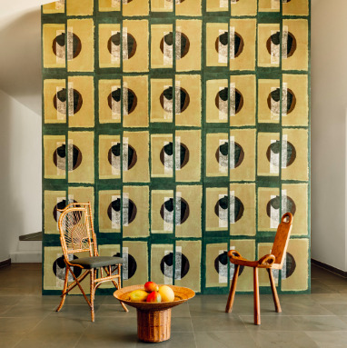 Kamer met Elitis Art Paper behang Izu RM 1030 05, twee designstoelen en een rotan bijzettafel met fruit.