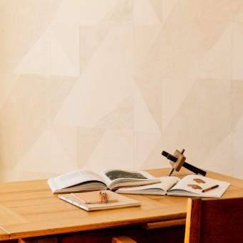 Houten bureau met open boeken en decoratieve voorwerpen voor een muur met Elitis Art Paper behang Tokara RM 1034 01.
