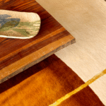 Detail van het Elitis Celeste vloerkleed TA 133 25 02 met warme kleurtinten naast een houten tafel.
