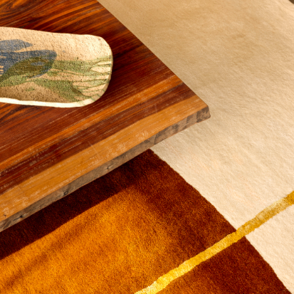 Detail van het Elitis Celeste vloerkleed TA 133 25 02 met warme kleurtinten naast een houten tafel.