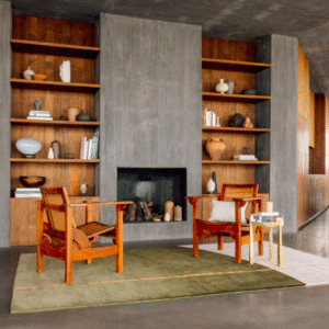 Moderne zithoek met twee houten stoelen op het Elitis Celeste vloerkleed TA 133 68 02 voor een betonnen open haard en ingebouwde houten boekenplanken.