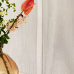 Detail van het Elitis Colonne RM 1044 01 Rayures Jumelles behang met een vaas met bloemen op de voorgrond.