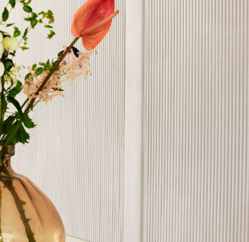 Detail van het Elitis Colonne RM 1044 01 Rayures Jumelles behang met een vaas met bloemen op de voorgrond.