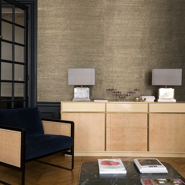 Stijlvolle woonkamer met Elitis Ecrin-behang, een rotan dressoir, moderne tafellampen en een fluwelen fauteuil.