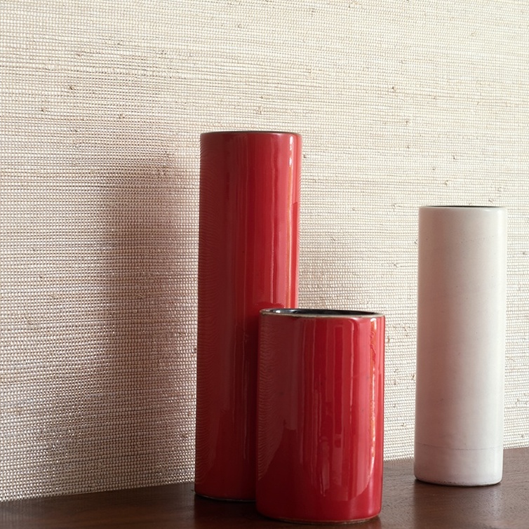 Drie cilindervormige vazen staan voor een muur met Elitis Ecrin behang met een natuurlijke textuur.