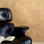 Zwarte leren loungefauteuil met open boek ervoor, tegen een wand met Elitis Empreintes RM 1040 15 behang uit de Marqueteries collectie.