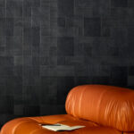Zwart Elitis Empreintes RM 1040 80 behang uit de Marqueteries collectie met houtnerfstructuur achter een bruine leren fauteuil en open notitieboek.