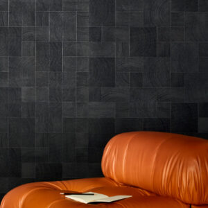 Zwart Elitis Empreintes RM 1040 80 behang uit de Marqueteries collectie met houtnerfstructuur achter een bruine leren fauteuil en open notitieboek.