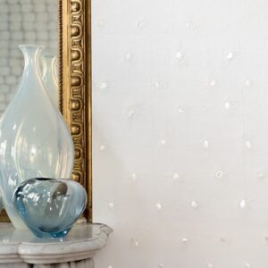 Glazen vazen op een marmeren tafel voor een gouden spiegel en een witte Elitis Ercin Naha-muur met subtiele structuur.