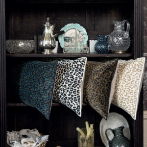 Vier Elitis Fauve-kussens met panterprint liggen op een donkere houten plank tussen decoratieve objecten en servies.