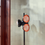 Detail van het Elitis Feuilles d'or RM 1041 42 behang uit de Marqueteries collectie met een moderne zwarte vloerlamp met oranje accenten.