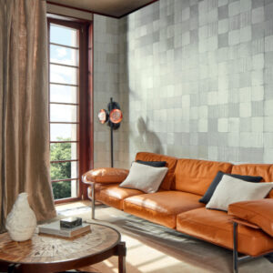 Moderne woonkamer met Elitis Feuilles d'or RM 1041 42 behang uit de Marqueteries collectie, een cognackleurige leren bank en grote raampartij.