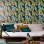 Woonkamer met Elitis Flower Power Alocasia TP 302 03 behang met tropisch bladmotief en een bank met gekleurde kussens.