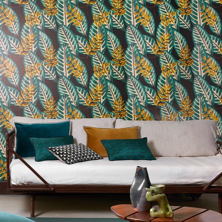 Woonkamer met Elitis Flower Power Alocasia TP 302 03 behang met tropisch bladmotief en een bank met gekleurde kussens.