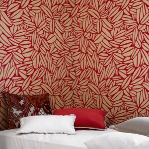 Behang Elitis Flower Power Succulente TP 301 05 met rood bladpatroon op een beige achtergrond achter een bed met sierkussens.
