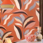 Oranje Elitis Flower Power-behang met abstracte botanische vormen in lichte en donkere tinten, gecombineerd met kleurrijke keramieken decorstukken op de voorgrond.