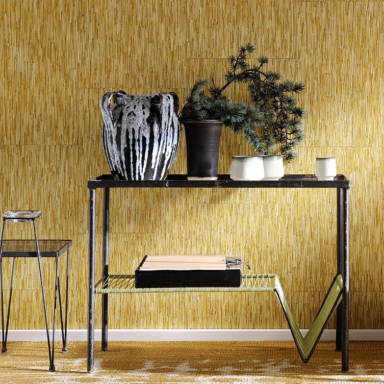 Zwarte metalen tafel met keramiek en planten tegen een wand bekleed met Elitis Formentera La casa de paja strostructuurbehang.