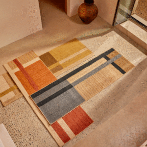 Modern Elitis Gustave TA 137 vloerkleed met geometrisch patroon in warme aardetinten en zwart, gelegd in een minimalistisch interieur.