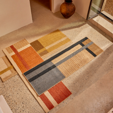 Modern Elitis Gustave TA 137 vloerkleed met geometrisch patroon in warme aardetinten en zwart, gelegd in een minimalistisch interieur.