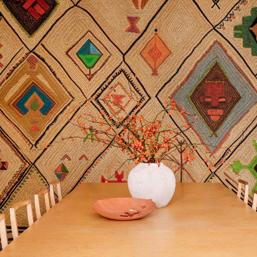 Eettafel met een witte vaas en oranje takken voor een wand bekleed met Elitis Hydra Lin Brodés VP 957 01 behang met kleurrijke geometrische patronen.