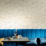 Moderne zithoek met blauwe fluwelen bank en Elitis Indiana-1 behang met subtiele kleurrijke strepen.