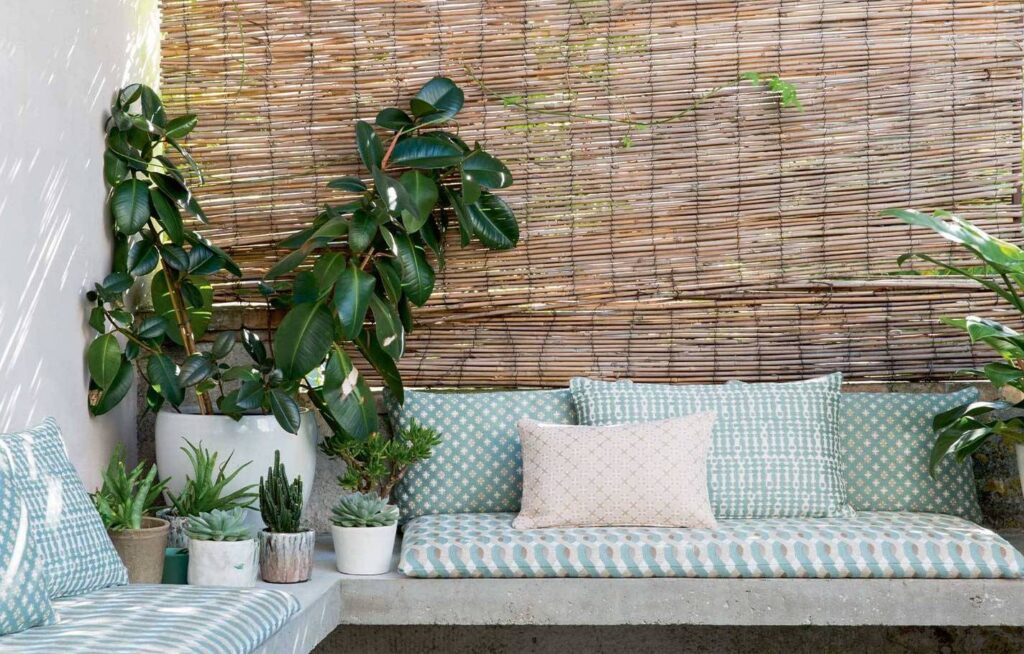 Stijlvolle zithoek met Elitis Iseo outdoorstof, omringd door planten en een bamboe wand bij Buningh Wonen.