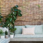 Stijlvolle zithoek met Elitis Iseo outdoorstof, omringd door planten en een bamboe wand bij Buningh Wonen.