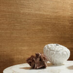 Witte vaas en rozenkwartsdecoratie op een marmeren tafel voor een goudkleurige Elitis Kosa Silk Metal VP 935 91 wandbekleding.