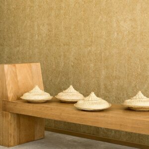 Houten bank met vier gevlochten manden tegen een goudkleurige Elitis Laca Salvaje muur.