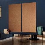 Twee grote panelen met Elitis Nacres Metal VP 949 93 wandbekleding hangen aan een donkerblauwe muur in een stijlvol interieur.