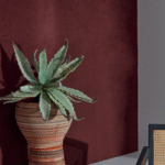 Een plant in een aardetinten pot staat voor een donkerrood Elitis Parthenon RM 1045 70 Rayures Jumelles behang.