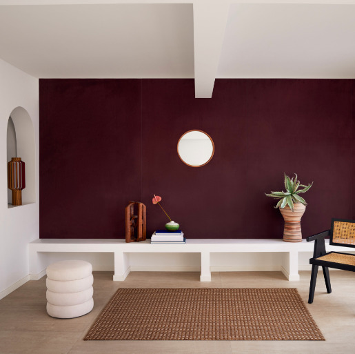Moderne woonkamer met Elitis Parthenon RM 1045 70 bordeauxrood behang, witte meubels en minimalistische decoratie.